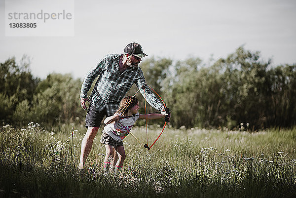 Vater hilft Tochter bei der Verwendung von Pfeil und Bogen auf Grasfeld