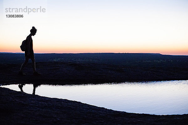 Seitenansicht der Silhouette einer Frau  die bei Sonnenuntergang am Teich auf dem Feld spazieren geht