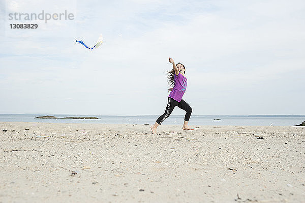 Mädchen spielt mit Drachen am Strand gegen den Himmel