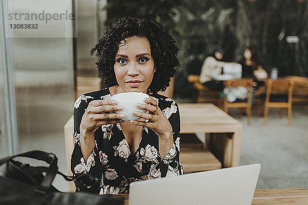 Porträt einer Frau  die Kaffee trinkt  während sie an einem Laptop-Computer am Tisch im Café sitzt