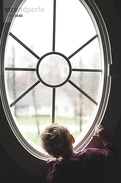 Rückansicht eines kleinen Jungen  der zu Hause durch ein Fenster schaut