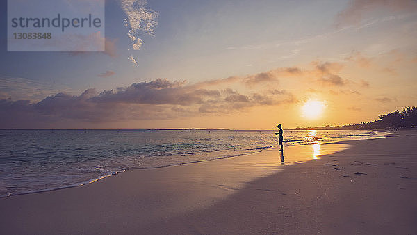 Seitenansicht des Silhouettenjungen  der bei Sonnenuntergang am Strand gegen den Himmel steht