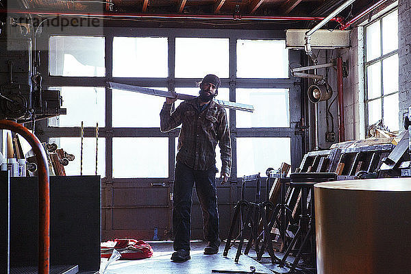 Porträt eines Arbeiters  der Metallplanken in der Werkstatt trägt