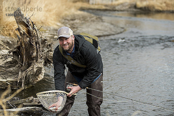 Lächelnder Mann  der im Fluss stehend Fische aus dem Falterfischernetz entfernt