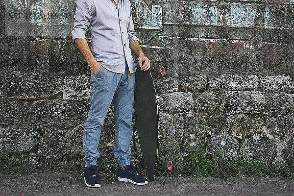 Niedriger Abschnitt eines Mannes  der ein Skateboard hält  während er an der Wand steht