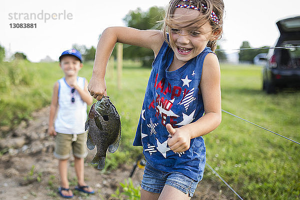 Verspielte Schwester mit gefangenem Fisch  während der Bruder im Hintergrund steht