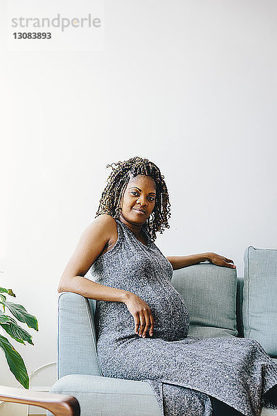Porträt einer schwangeren Frau  die zu Hause auf einem Sofa an der Wand sitzt