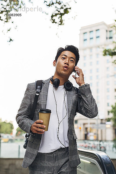 Geschäftsmann spricht mit einem Smartphone  während er in der Stadt einen Einwegbecher hält