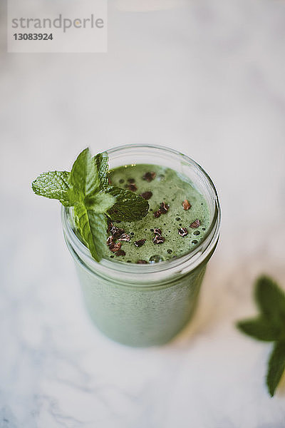 Hochwinkelansicht eines Smoothie mit Minzeblättern und Kakaofedern in einem Steinmetzglas auf dem Tisch