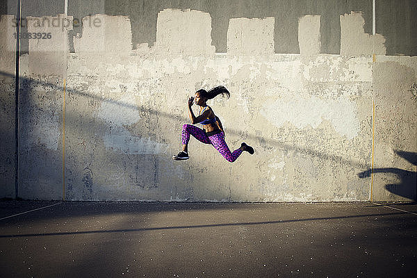 Seitenansicht einer Sportlerin  die in der Luft gegen eine Wand springt
