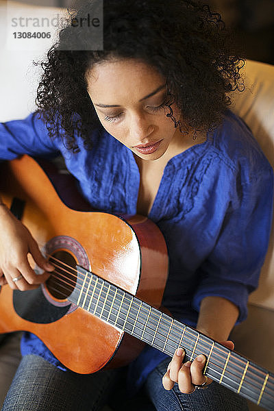 Hochwinkelansicht einer Frau  die auf dem Sofa sitzend Gitarre übt