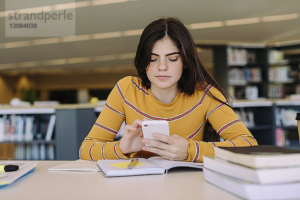 Frau benutzt Mobiltelefon während des Studiums in der Bibliothek