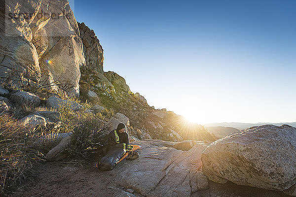 Wanderer sitzt auf einer Felsformation bei Bergen gegen klaren Himmel an einem sonnigen Tag