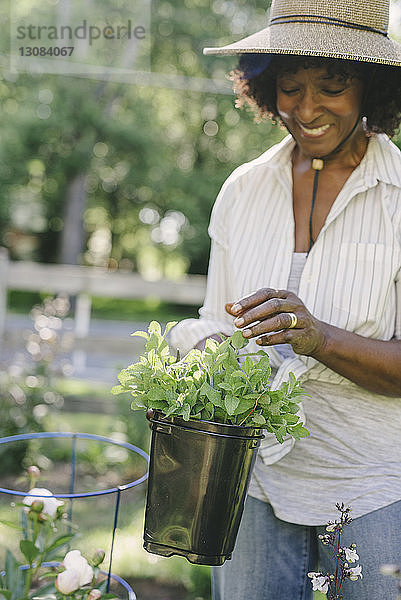 Glückliche reife Frau hält Topfpflanze im Garten