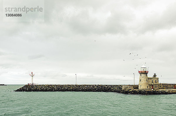 Leuchtturm am Meer vor bewölktem Himmel