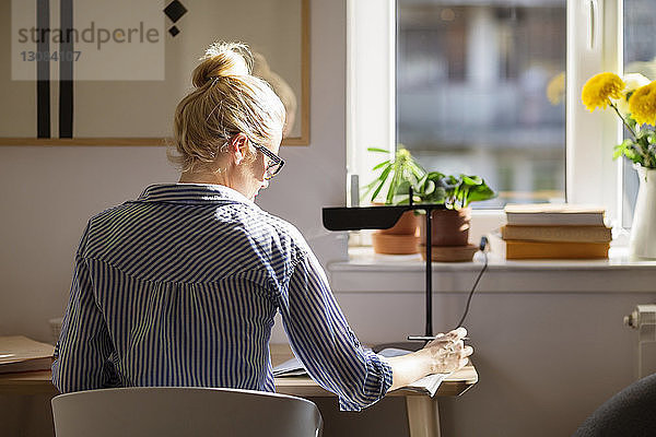 Rückansicht einer Frau  die am Tisch sitzend schreibt