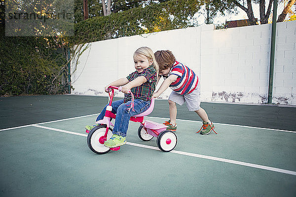Junge schiebt Schwester auf Dreirad im Hof