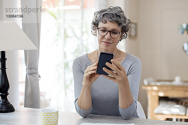 Reife Frau benutzt Smartphone auf dem Tisch zu Hause