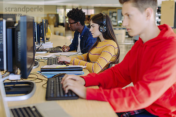 Freunde nutzen Desktop-Computer  während sie in der Bibliothek sitzen