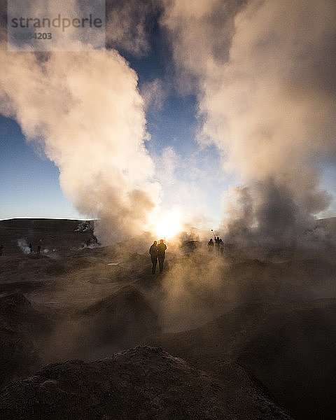 Silhouetten von Menschen  die bei Sonnenuntergang an der Vulkanlandschaft gegen den Himmel stehen