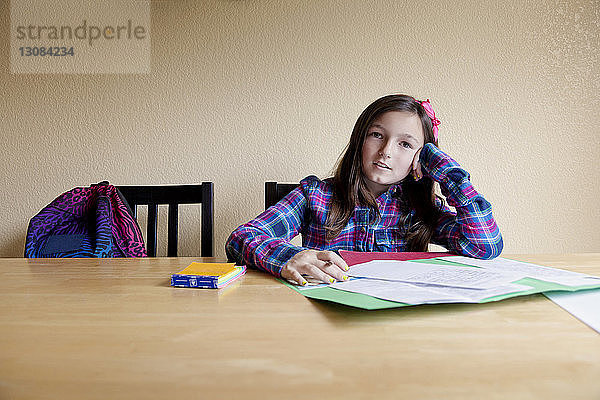 Porträt eines Mädchens  das lernt  während es zu Hause auf einem Tisch an der Wand sitzt