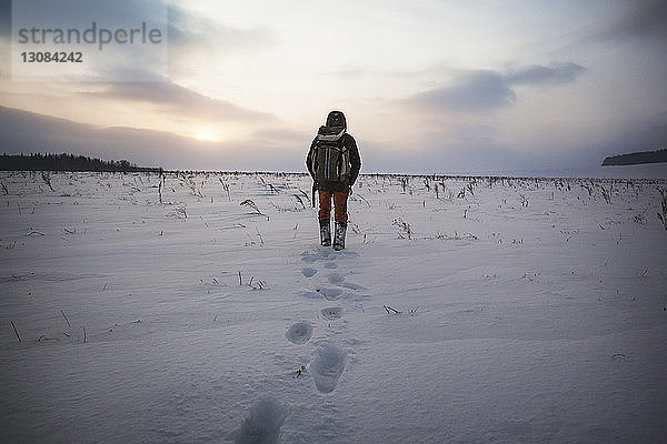 Rückansicht eines Mannes  der auf einem schneebedeckten Feld gegen den Himmel läuft