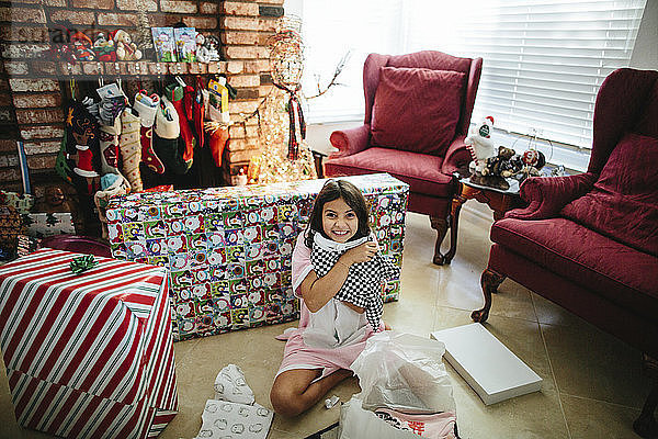 Porträt eines glücklichen Mädchens mit Weihnachtsgeschenk  das zu Hause auf dem Boden sitzt