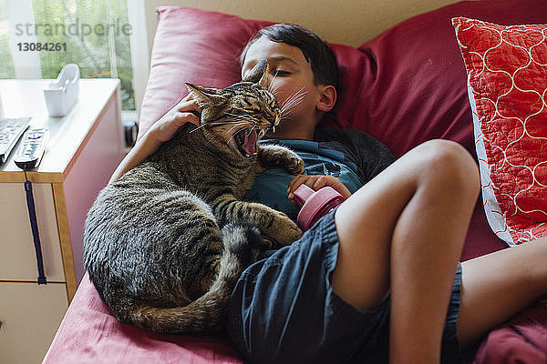 Schrägansicht eines Jungen mit Katze  der zu Hause auf dem Bett liegt