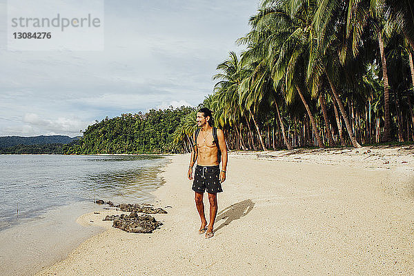 Wanderer ohne Hemd mit Rucksack am Strand stehend