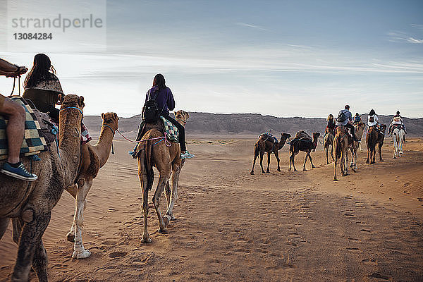 Touristen reiten auf Kamelen in der Wüste gegen den Himmel