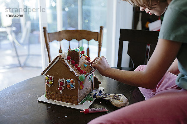 Mädchen schmückt Lebkuchenhaus auf dem heimischen Tisch