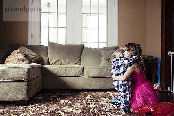 Seitenansicht eines Mädchens  das seinen Bruder im Wohnzimmer umarmt