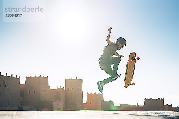 Mann in voller Länge  der bei sonnigem Wetter einen Stunt auf Skateboard gegen die Burg vorführt