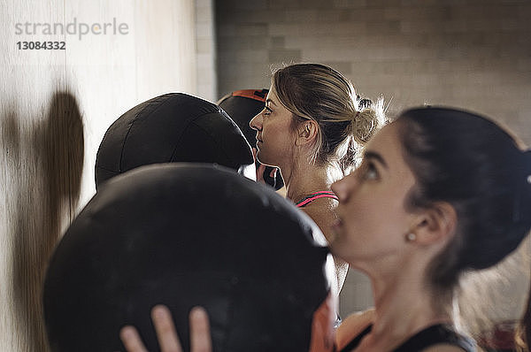 Seitenansicht von entschlossenen Sportlerinnen  die mit Medizinbällen im Fitnessstudio trainieren