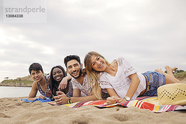 Porträt von fröhlichen Freunden auf einer Decke am Strand liegend