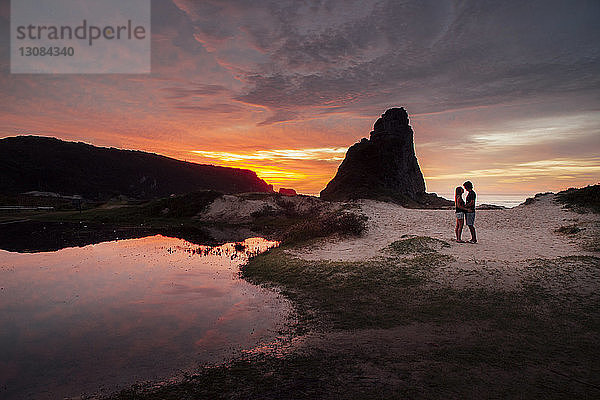 Romantisches Paar  das bei Sonnenuntergang auf Sand gegen den Himmel steht