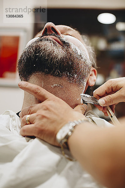 Abgetrennte Hände eines Friseurs beim Rasieren eines männlichen Kunden im Salon