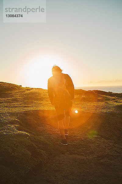 Rückansicht eines männlichen Wanderers  der bei Sonnenuntergang auf einem Hügel läuft