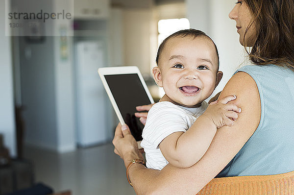 Mutter trägt Baby Junge in Tragetasche  während sie einen Tablet-Computer benutzt