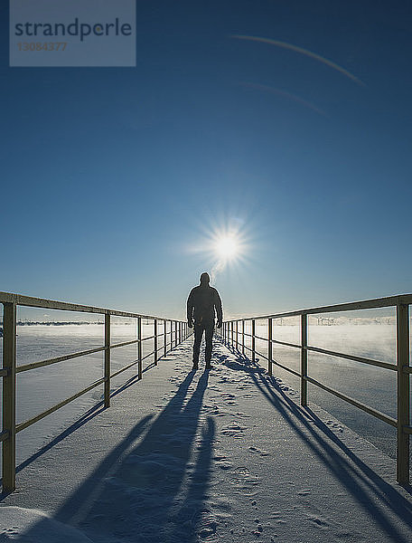 Rückansicht eines Mannes  der auf einem schneebedeckten Pier über einem zugefrorenen See steht  gegen den Himmel