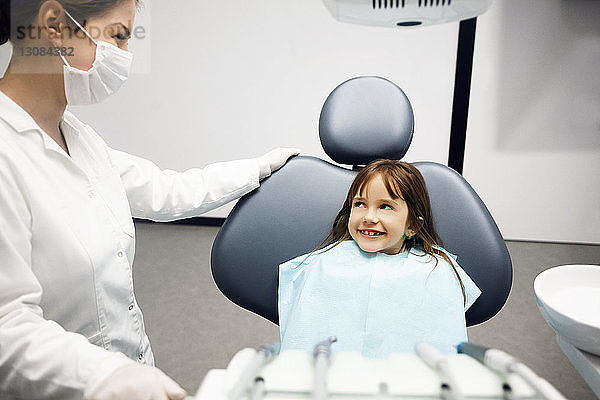 Lächelndes Mädchen schaut den Zahnarzt an  während es in der Klinik sitzt