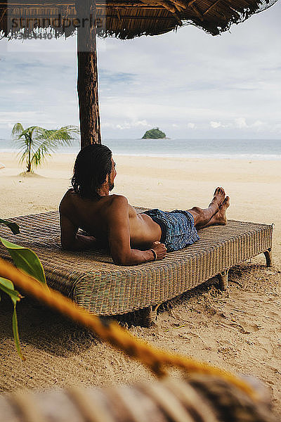 Rückansicht eines hemdlosen Mannes  der sich am Strand im Bett ausruht