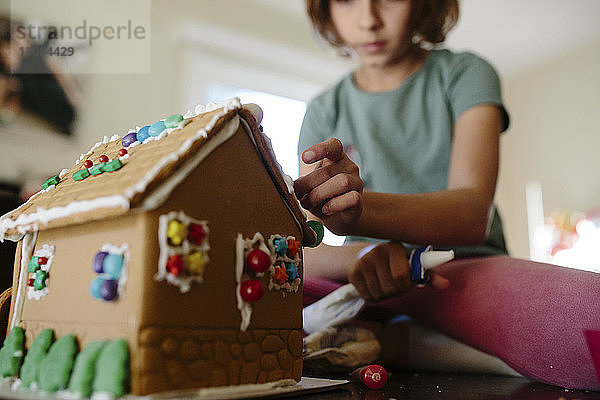 Niedrigwinkelansicht eines Mädchens  das zu Hause Lebkuchenhaus auf dem Tisch macht