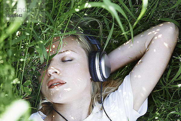 Draufsicht einer Frau mit geschlossenen Augen  die Musik hört  während sie mitten im Gras auf dem Feld liegt