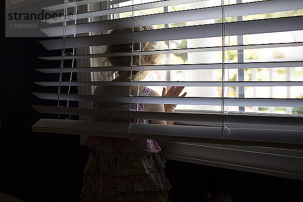 Mädchen schaut durch Fenster  während sie zu Hause steht