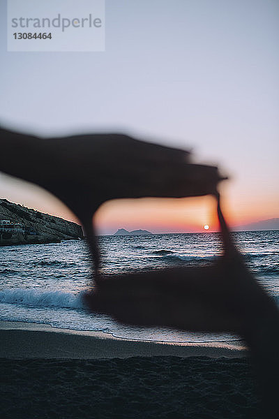 Sonne durch den Rahmen der Hände gegen den Himmel am Strand gesehen