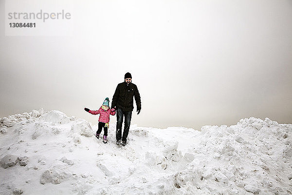 Grossvater und Enkelin gehen auf schneebedecktem Feld vor bewölktem Himmel