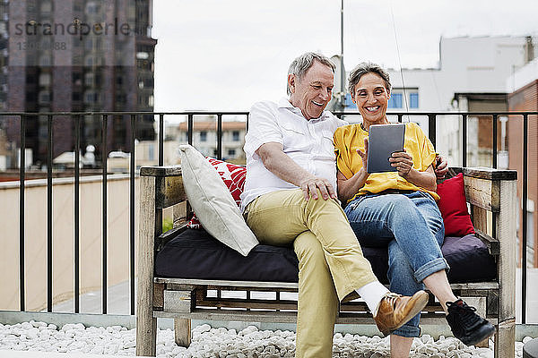 Glückliches älteres Ehepaar benutzt Tablet-Computer  während es auf einer Bank auf der Terrasse sitzt