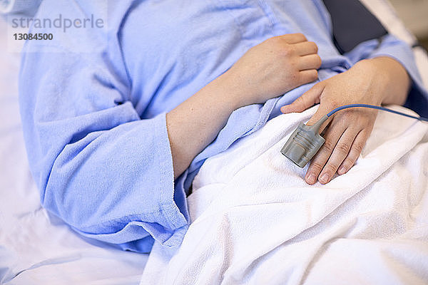 Mittelsektion einer Patientin mit Pulsoxymeter  die im Krankenhaus auf dem Bett liegt