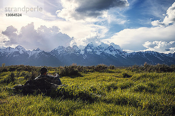 Mann liest Buch  während er sich auf Grasfeld vor bewölktem Himmel entspannt